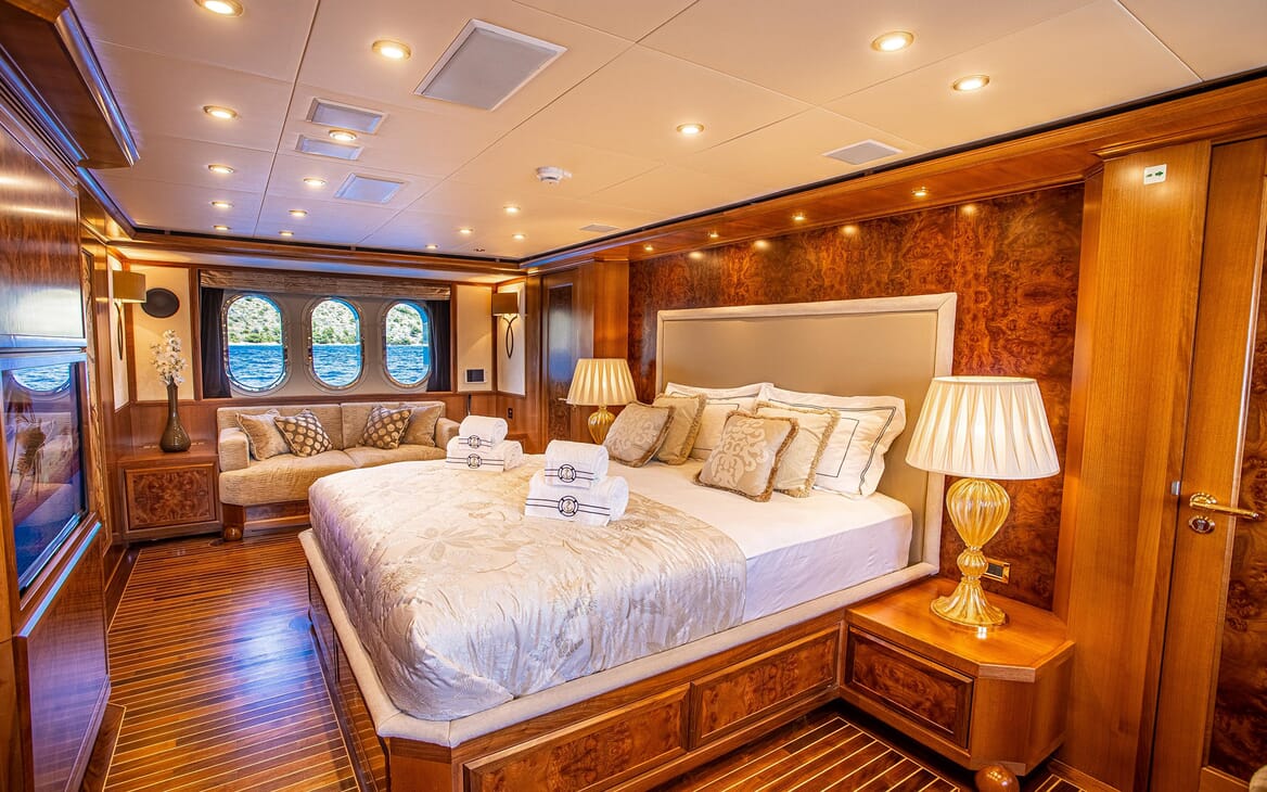 Motor yacht Milaya master suite with gold and white bed linen and soft sofa under window