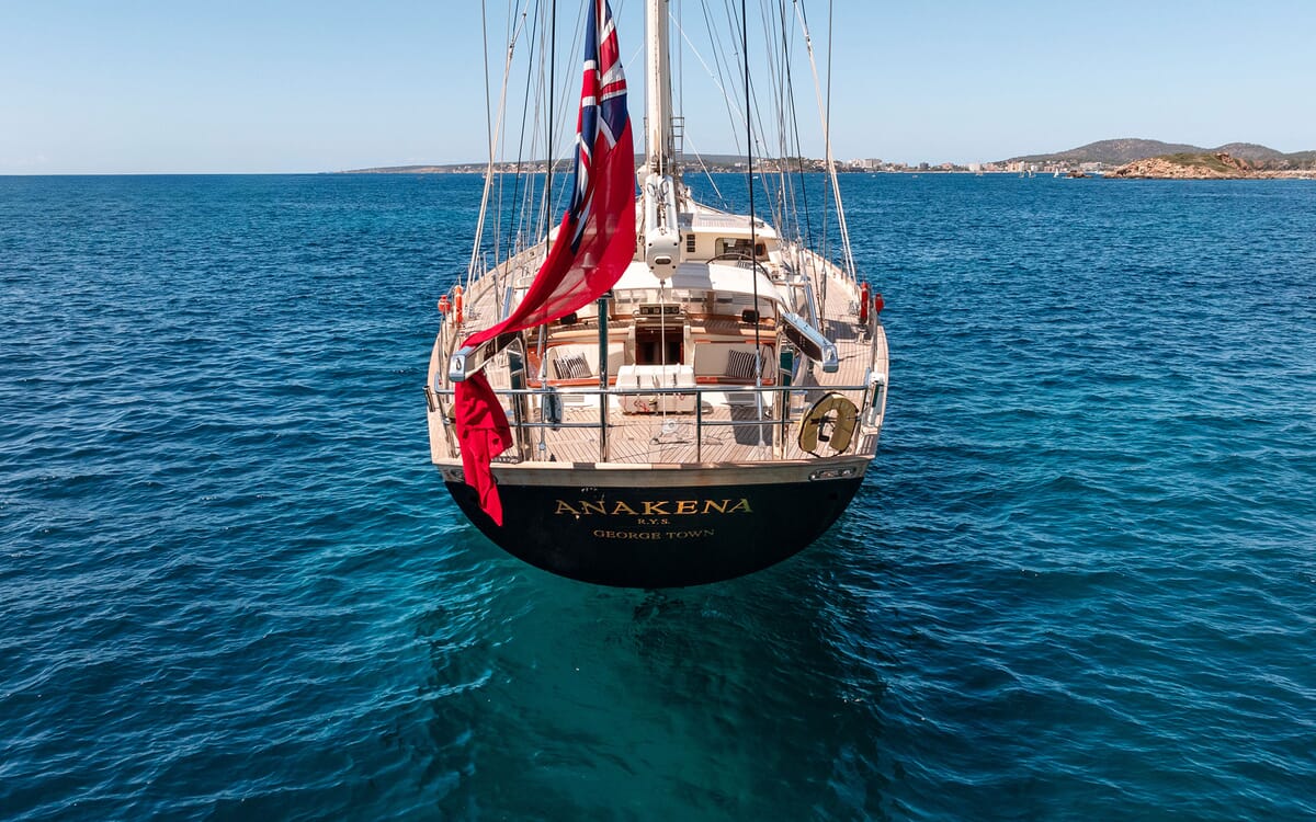 Luftaufnahme der Segelyacht ANAKENA auf See. Das Bild zeigt das Heck mit seinem Namen, eine Union Jack Flagge und das Holzdeck.
