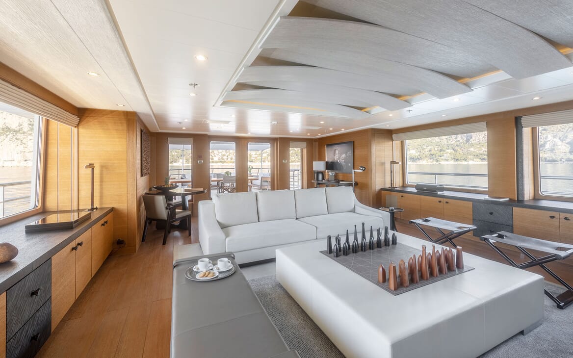 Motor yacht Spirit interior living room shot with grey furnishings, wood surrounding and large chess board in centre of room
