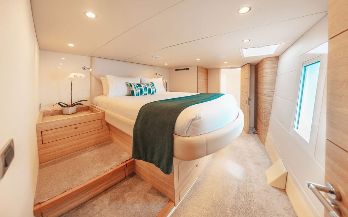 Motor yacht SAMARA bedroom with stairs leading up to large double bed with white linen and turquoise details, cream soft furnishings throughout