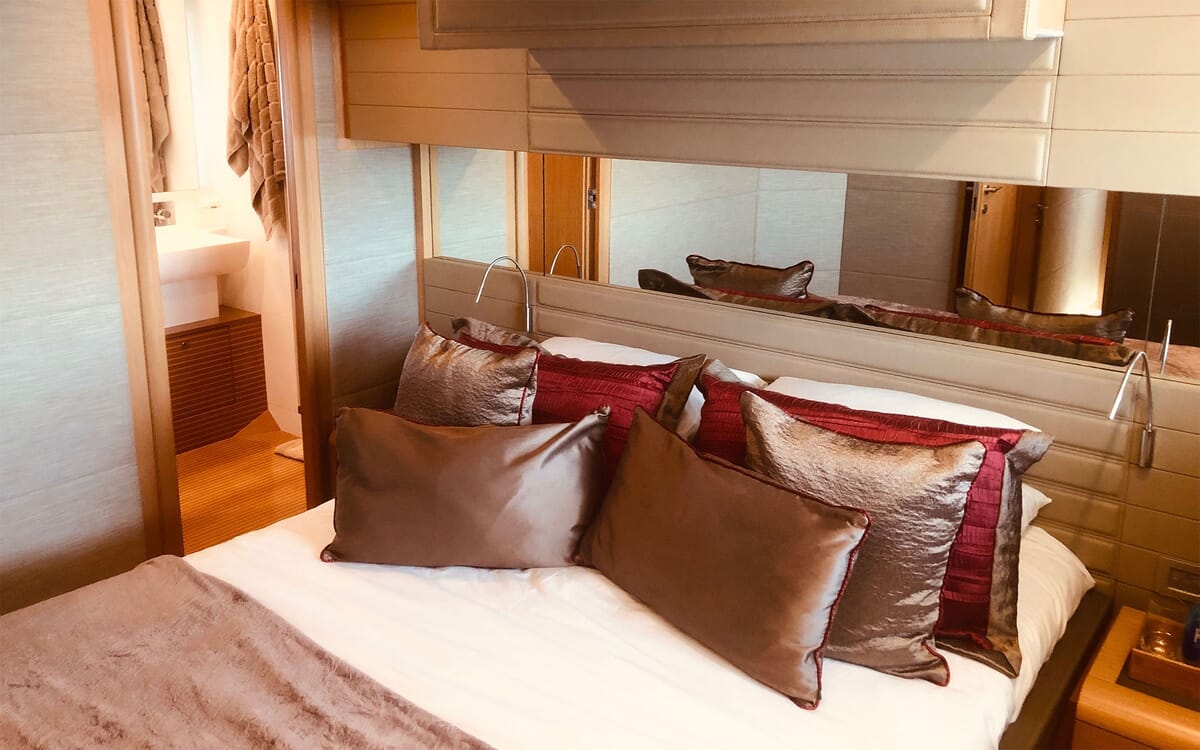 Interior of yacht JPS, a 24.71m vessel, featuring a luxurious bedroom. Shows a bed with pillows and a glimpse of the bathroom.