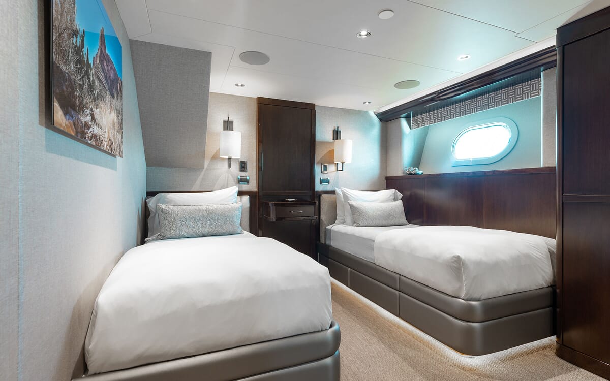 Interior of the FIGARO yacht features a well-appointed guest room with twin beds, modern lamps, and a porthole window.