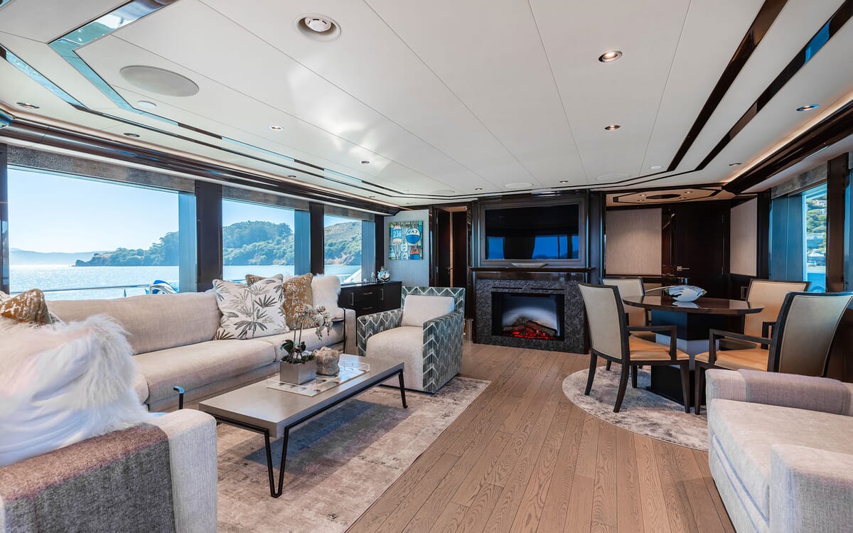 Interior of the FIGARO yacht, featuring a luxurious living area with a fireplace, large windows overlooking the sea, and modern furniture.