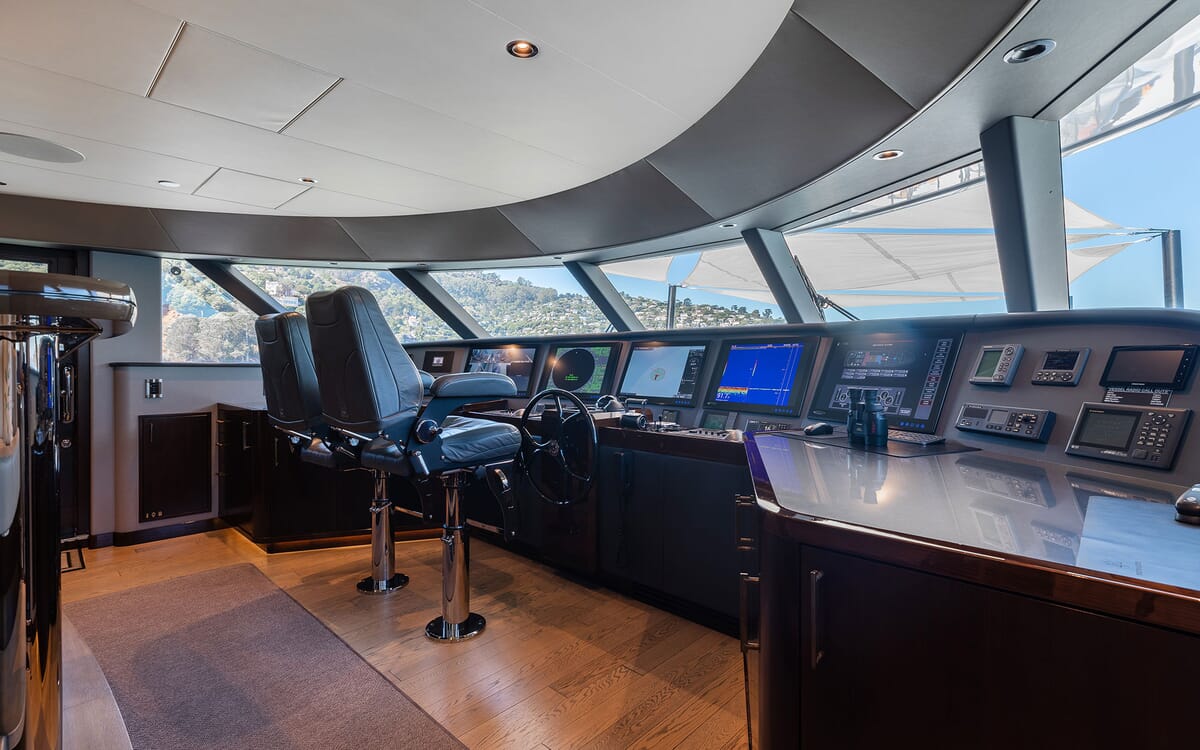 Interior shot of the FIGARO yacht's bridge featuring navigation screens, a steering wheel, and pilot chairs. The setting shows open sea views.