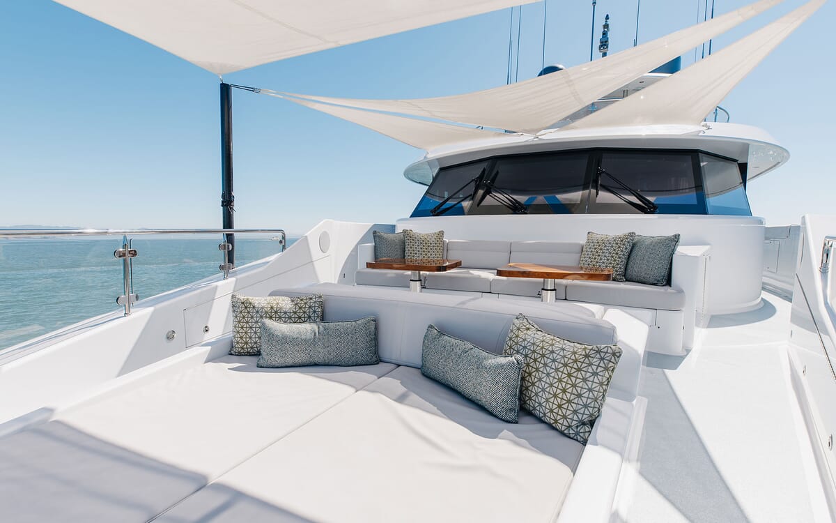 Exterior of the 39.62m yacht FIGARO. A sunny day view from the upper deck shows seating, pillows, and a sunshade, with the sea in the background.