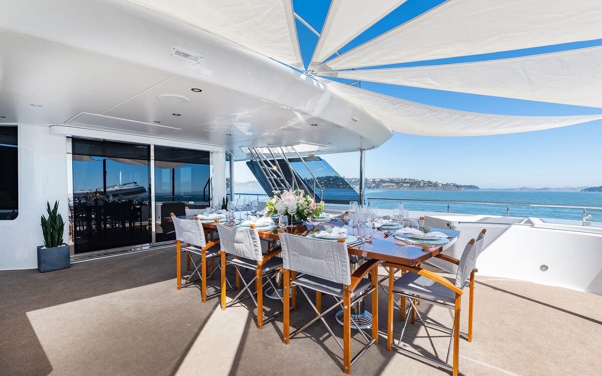 Outdoor dining area of the 39.62m yacht FIGARO, featuring a beautifully set table, with ocean views under a stylish sun shade.