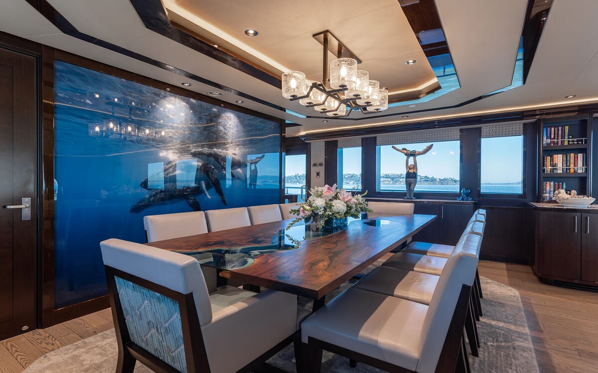 Interior of the FIGARO yacht. Features a dining area with a large wooden table, decorative lighting, and an underwater mural on the wall.