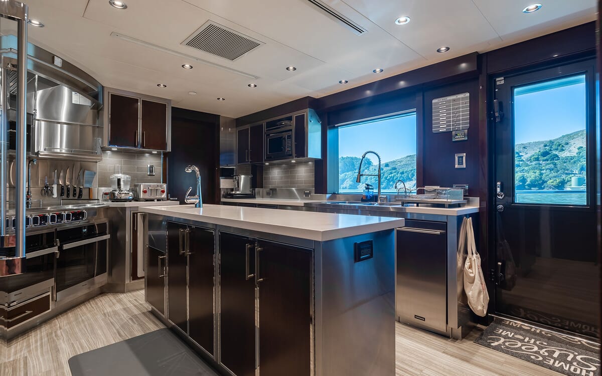 Interior view of the FIGARO yacht kitchen, featuring stainless steel appliances, a large island, and a scenic view through the window.