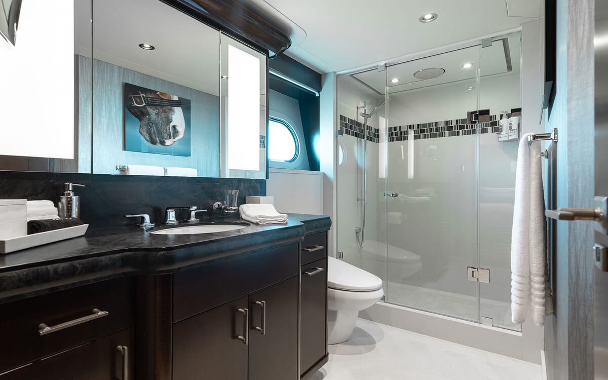 Interior view of a bathroom onboard the yacht FIGARO. Features include a dark vanity with sink, glass shower, and a porthole.