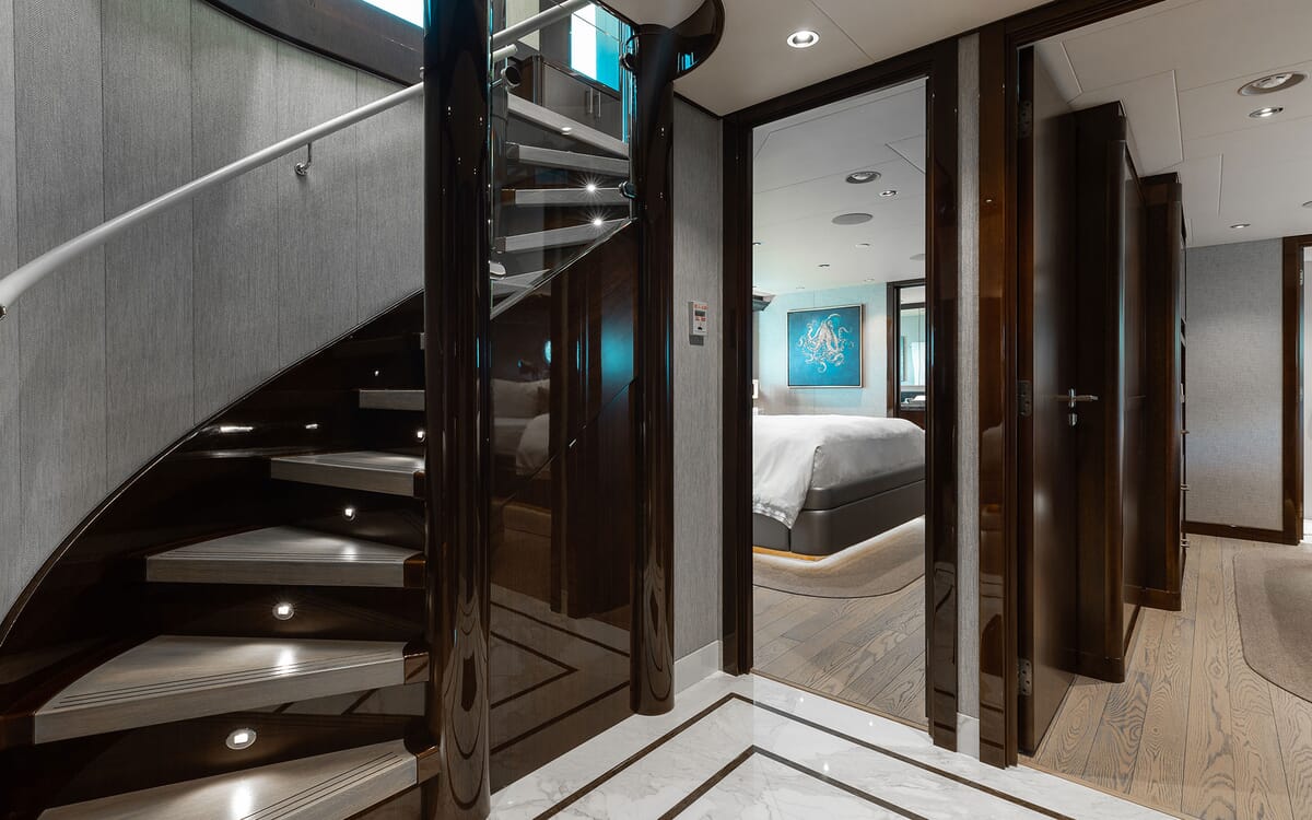 Interior view of yacht FIGARO, showcasing a spiral staircase with illuminated steps and a bedroom entrance visible, featuring artwork.