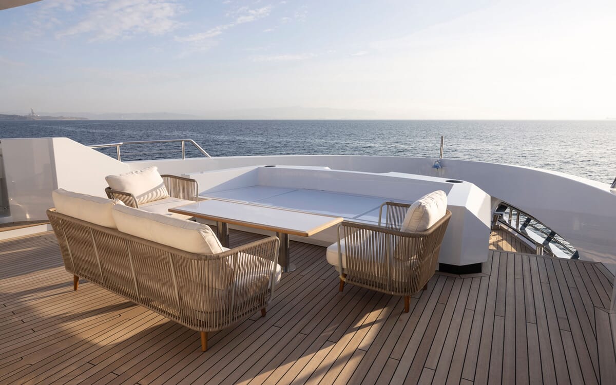 El BEE YACHT, un yate de 35,42 m, muestra su cubierta con asientos y una mesa, con vistas al mar. Una vista relajada desde una cubierta.