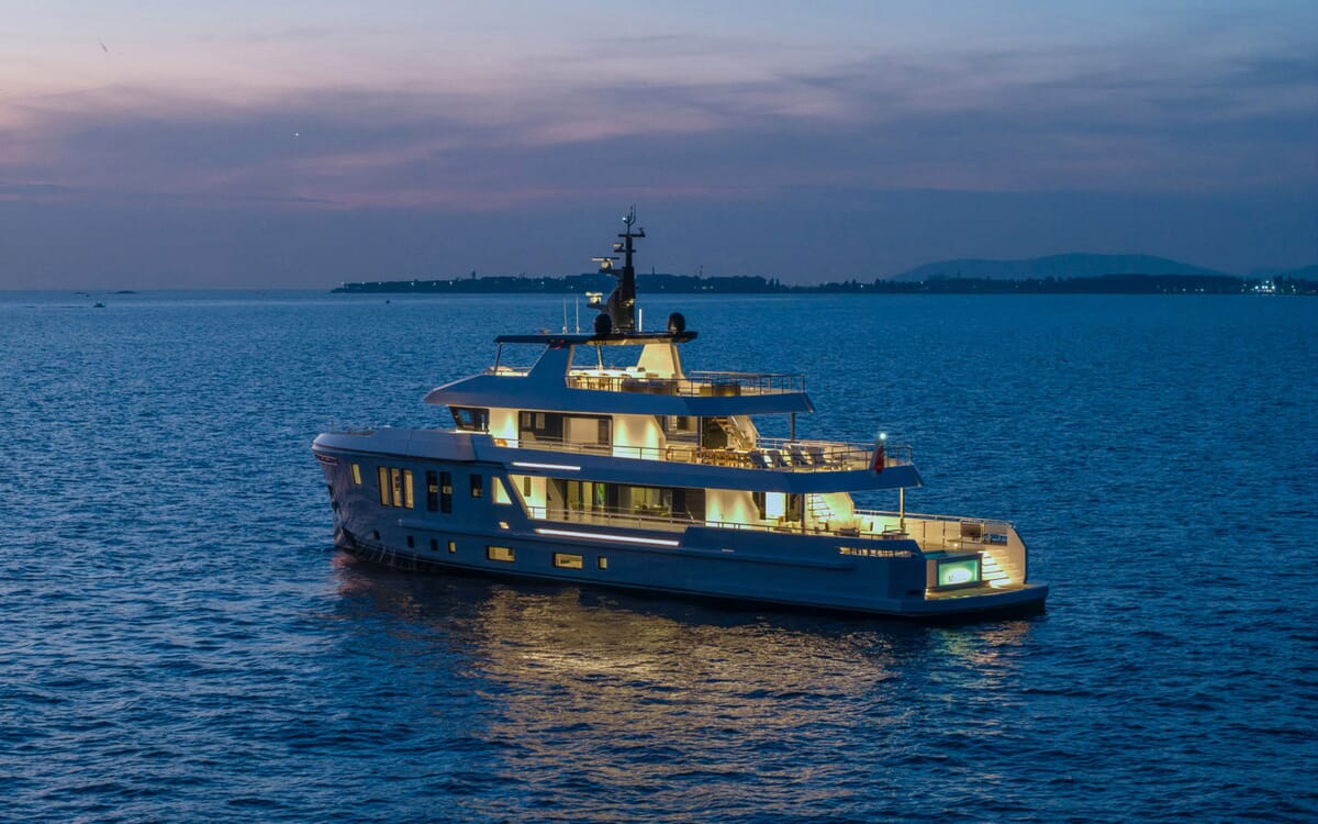 Vista lateral del BEE YACHT, un yate de 35,42 m, en el mar al anochecer. El yate está iluminado, mostrando sus características exteriores y de cubierta.