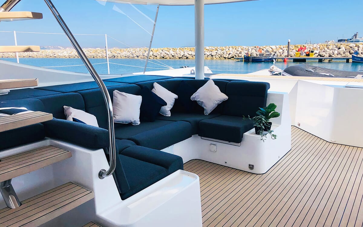 Blick auf das Deck der 23,42 m langen Yacht MAHAL KO mit einer Sitzecke mit blauen Kissen und weißen Polstern, die auf See liegt.