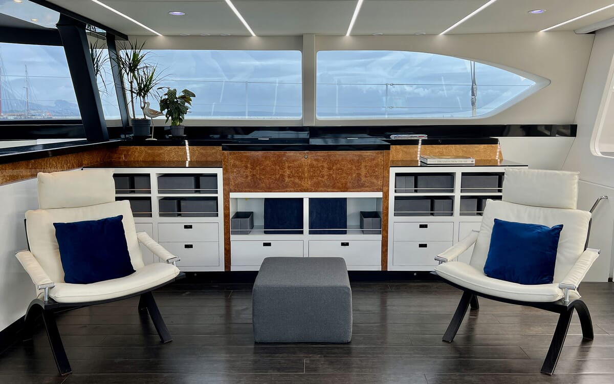 Innenansicht der Jacht MAHAL KO. Zur Ausstattung gehören weiße Sessel mit marinefarbenen Kissen, Holzschränke und große Fenster mit Aussicht.