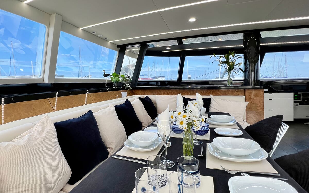 Innenaufnahme der Yacht MAHAL KO (23,42 m). Der Essbereich ist mit einem Tisch und Sitzgelegenheiten ausgestattet und bietet durch große Fenster einen Blick auf den Yachthafen.