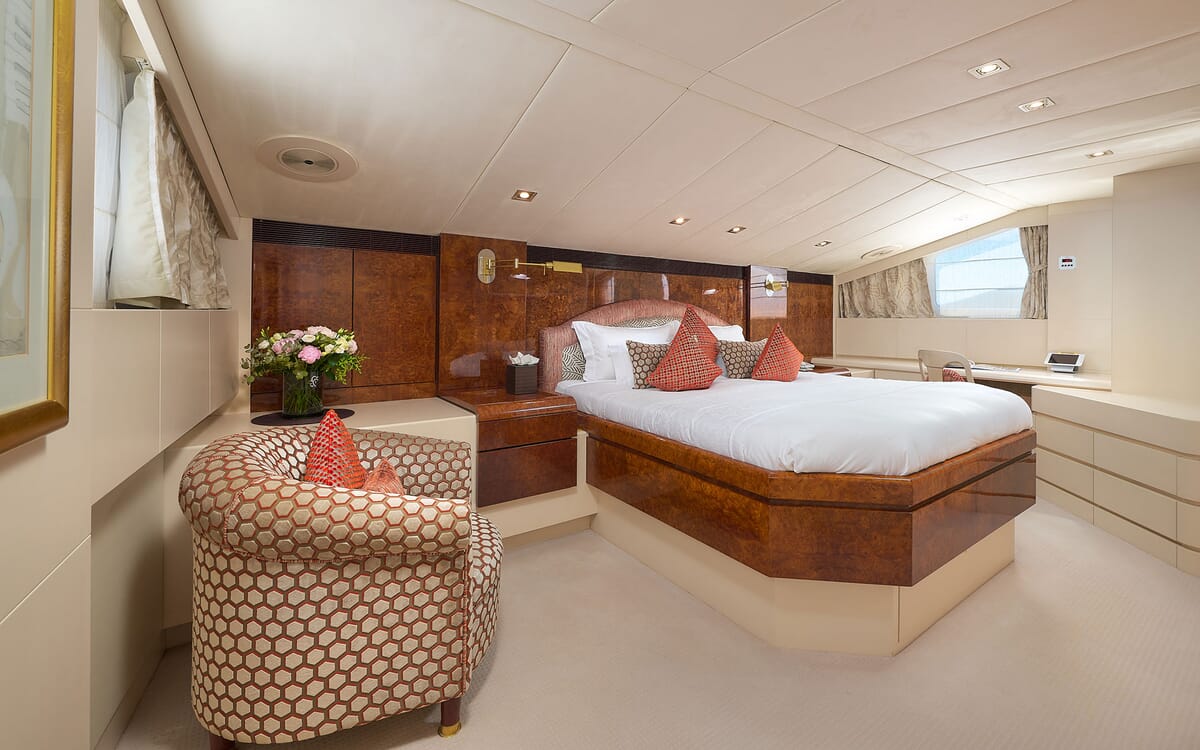 Interieur des Schlafzimmers der LADYSHIP Yacht mit großem Bett, gemustertem Sessel und Holzakzenten. Ein gut beleuchteter, luxuriöser Raum.