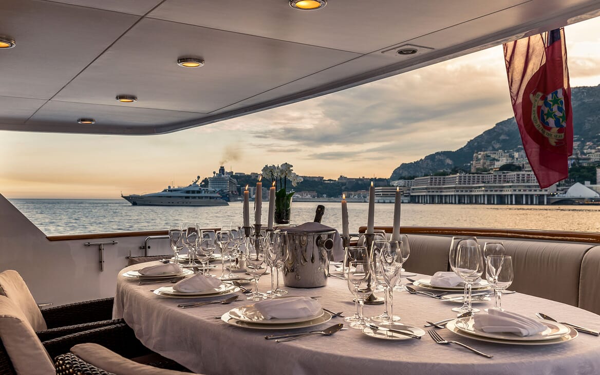 Motor yacht Superfun alfresco dining area with laid table and candles, views of monaco shoreline at dusk