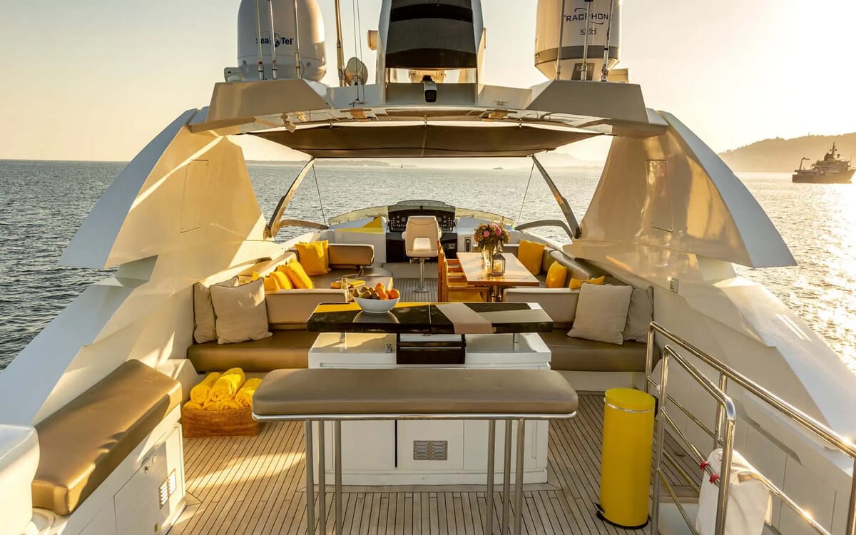 Rückansicht der Luxusyacht QUANTUM (28,41 m) auf See. Zur Ausstattung gehören ein geräumiges Deck mit Sitzgelegenheiten, Tischen und leuchtend gelben Akzenten.