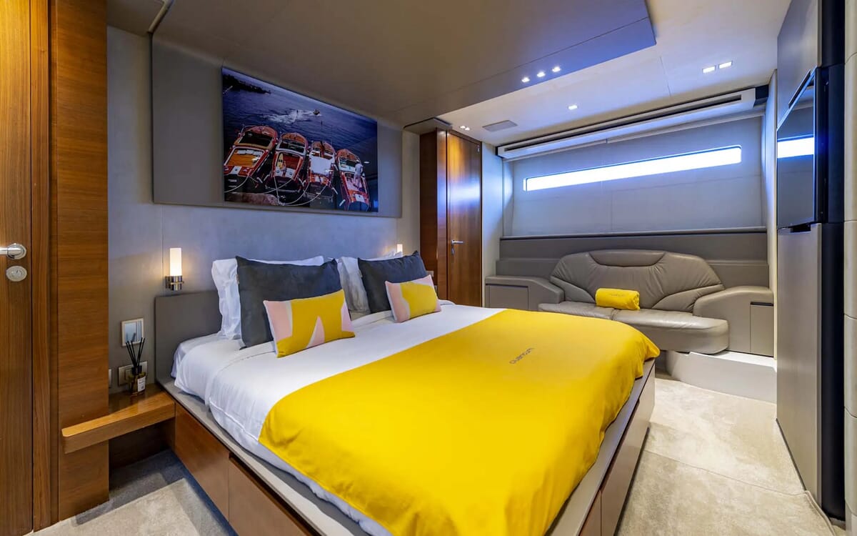 Innenaufnahme des Schlafzimmers der QUANTUM-Yacht, mit einem großen Bett mit gelber Bettwäsche, einem grauen Sofa und einem Gemälde über dem Bett.
