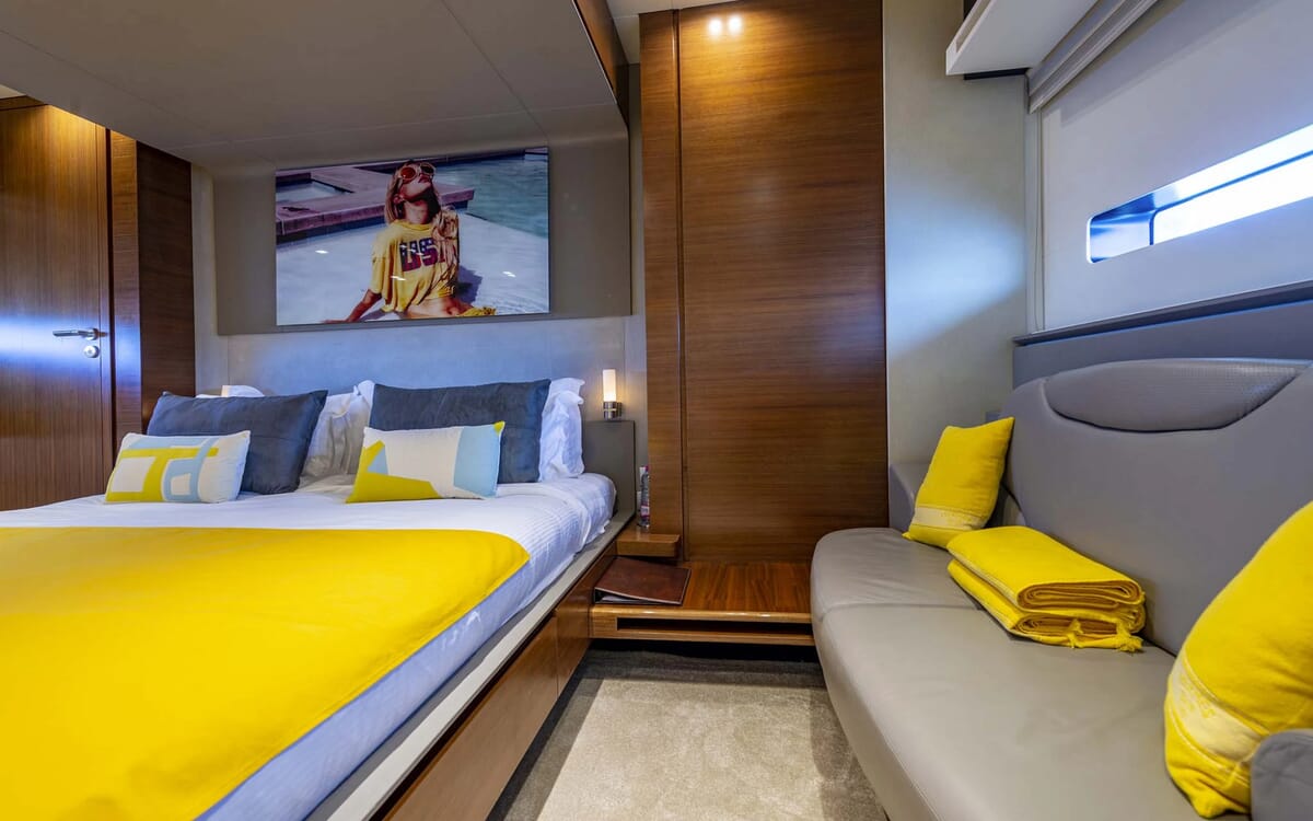 Das Innere der QUANTUM-Yacht zeigt ein Schlafzimmer mit einem Bett, einem Sofa und einem großen Fernseher. Die Einrichtung besteht aus Holzvertäfelung und einer leuchtend gelben Tagesdecke.