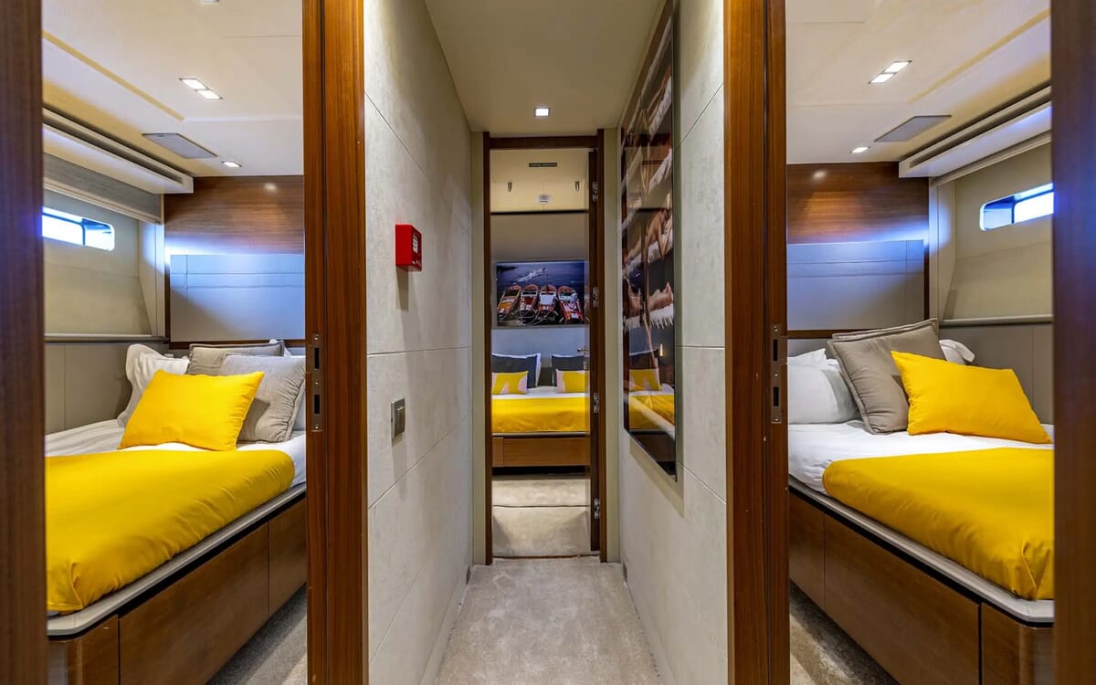 Innenansicht der QUANTUM-Yacht. Zu sehen sind Einzelbetten mit gelber Bettwäsche, getrennt durch einen Flur, der zu einem anderen Raum führt.