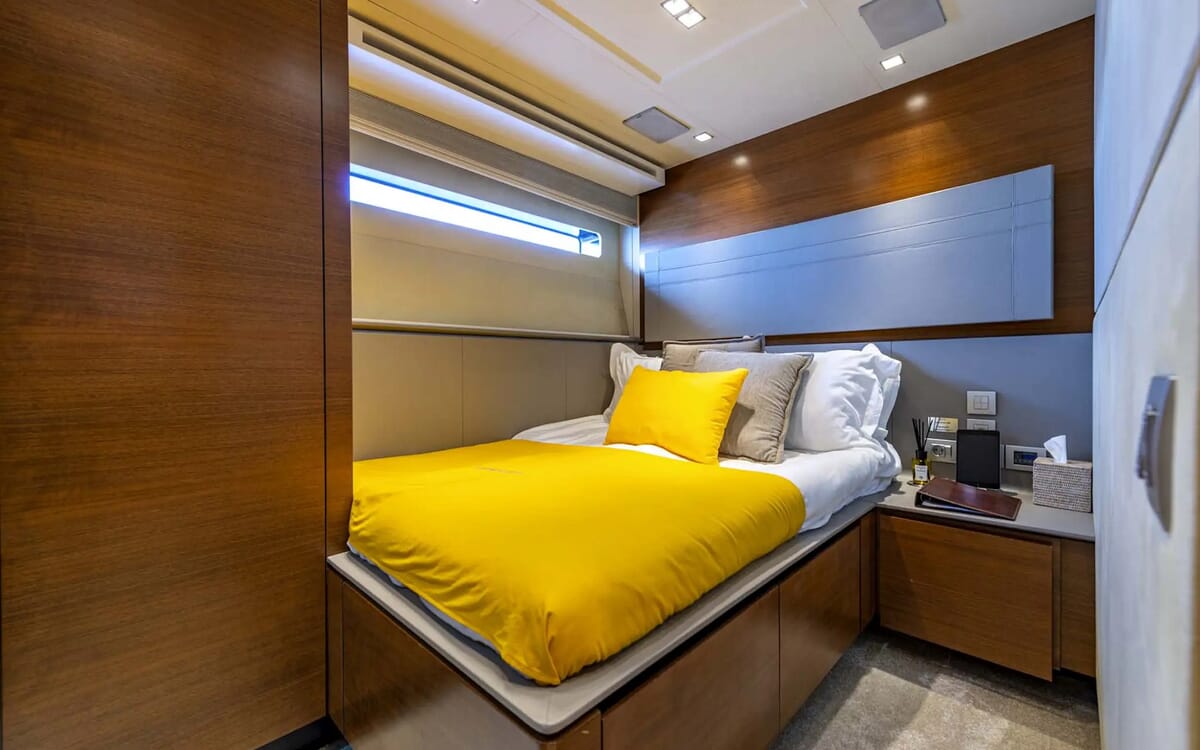 Das Innere der QUANTUM-Yacht zeigt ein Schlafzimmer. Das Bett ist mit leuchtend gelber Bettwäsche bezogen, die Wände und Schränke sind aus Holz.