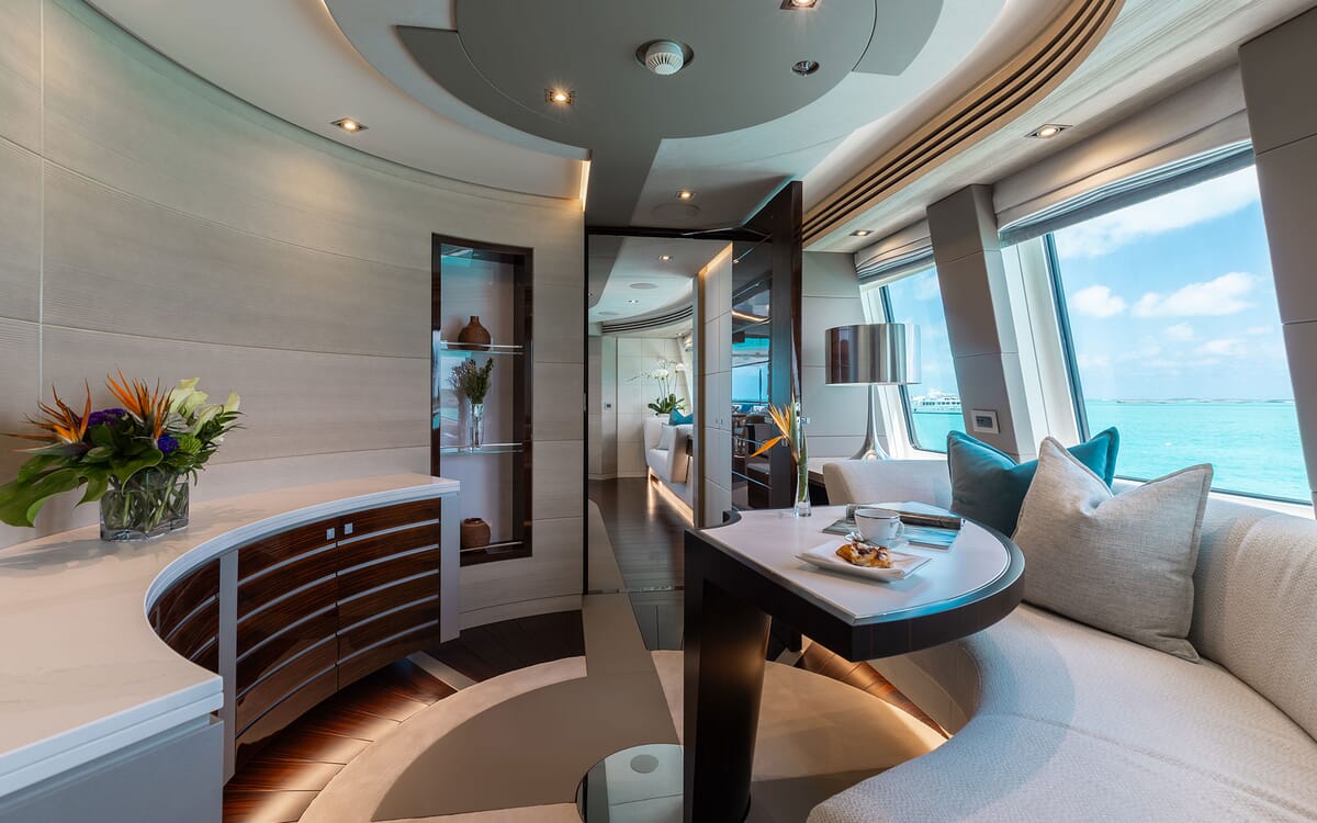 Innenansicht der ODYSSEA-Yacht. Mit einem geschwungenen Sitzbereich mit einem Tisch, einer Blumenauslage und einem Blick auf das Meer durch ein großes Fenster.