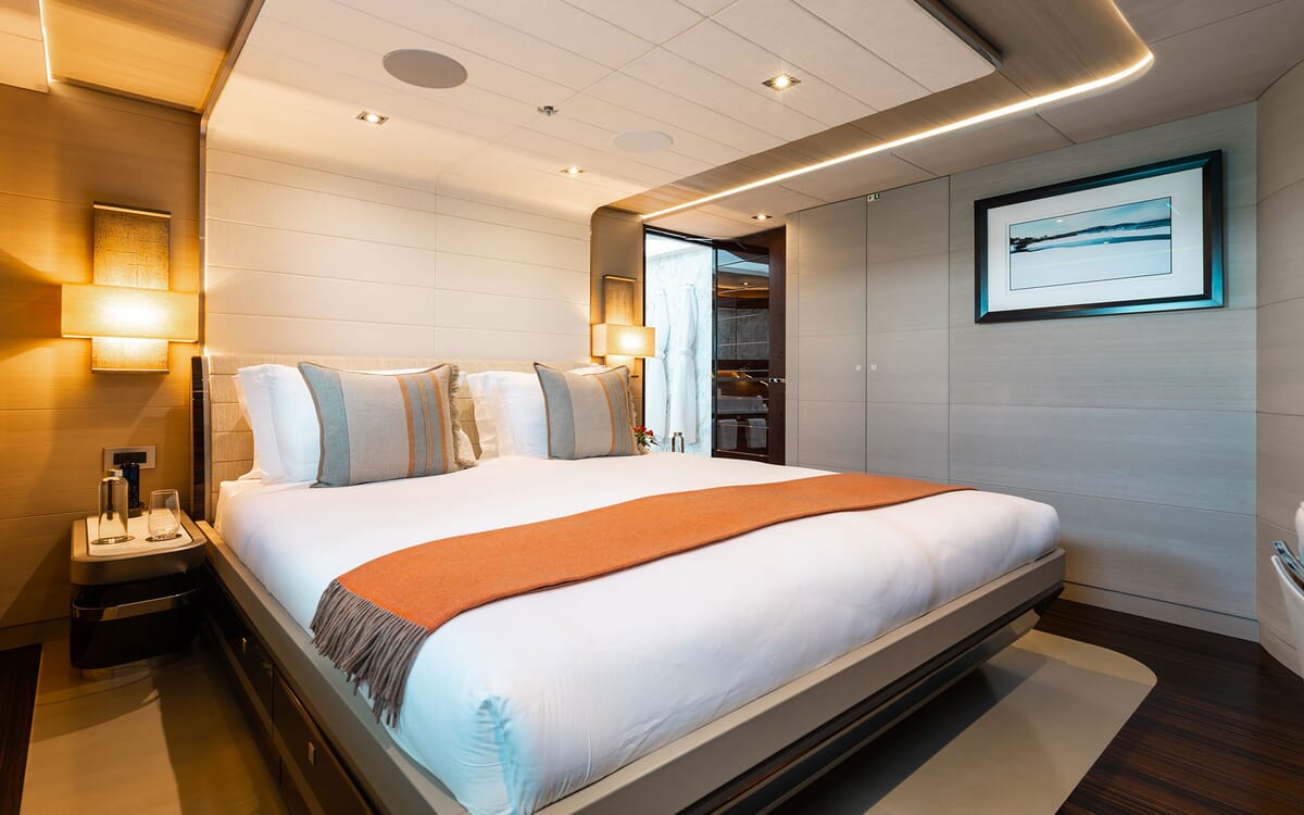 Das Innere der ODYSSEA Yacht. Das Schlafzimmer ist mit einem Kingsize-Bett mit orangefarbenen Akzenten, eingebauten Lampen und einem modernen gerahmten Kunstwerk ausgestattet.