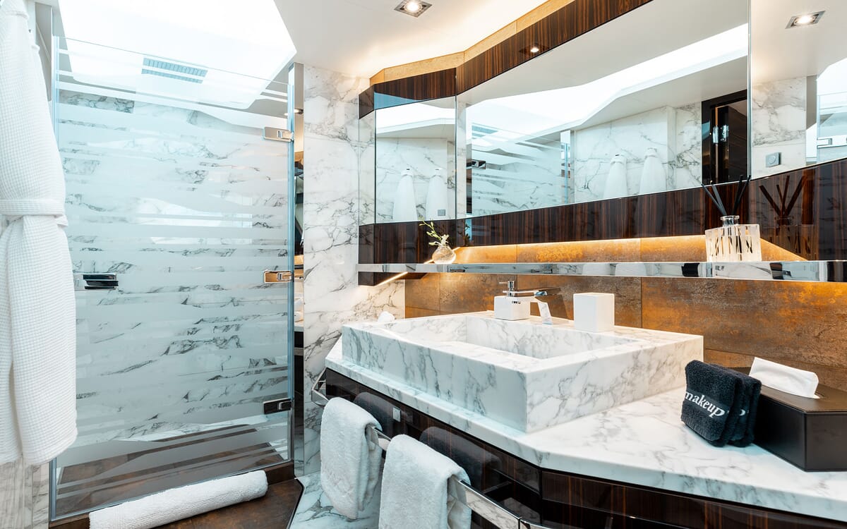 Das Innere des Badezimmers der ODYSSEA-Yacht. Zur Ausstattung gehören ein Marmorwaschbecken, eine begehbare Dusche und ein deckenhoher Spiegel. Luxuriöses, modernes Design mit Holzakzenten.