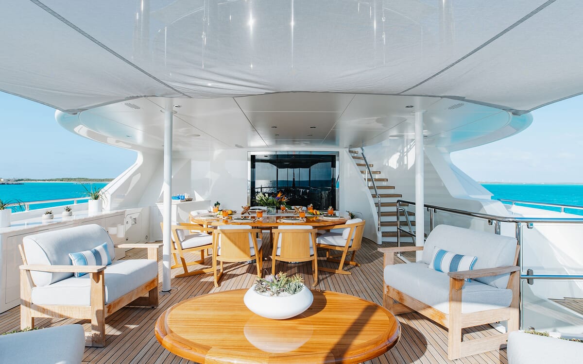 Ein luxuriöser Blick auf das Deck der Yacht ODYSSEA. Das Bild zeigt einen Esstisch und einen Sitzbereich mit einer wunderschönen Meereskulisse.