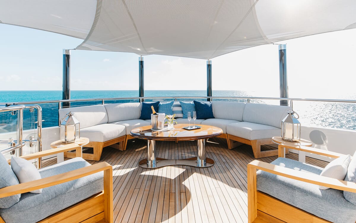 Die Yacht ODYSSEA, ein 46,71 m langes Schiff, verfügt über einen luxuriösen Lounge-Bereich im Freien mit Sitzgelegenheiten, einem Tisch und Blick auf das offene Meer.