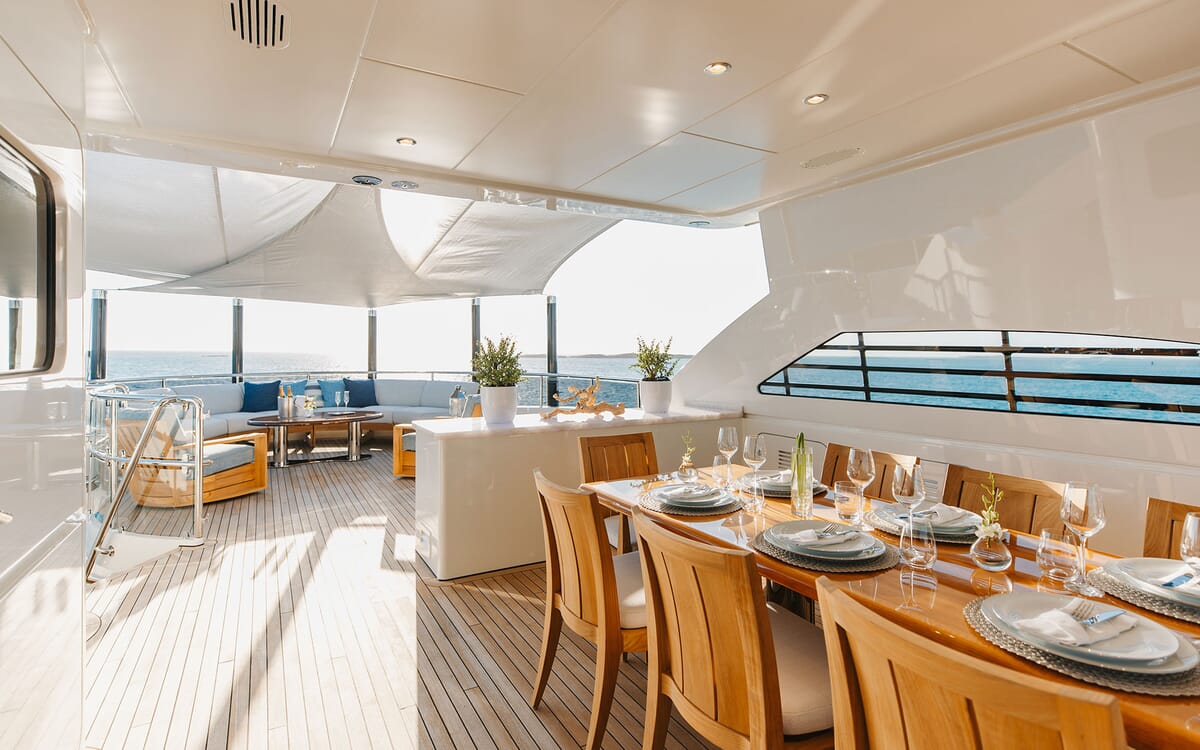 Der Essbereich der ODYSSEA Yacht im Freien mit einem langen Tisch für eine Mahlzeit mit Blick auf das Meer. Zur Ausstattung gehören ein Lounge-Bereich und viel Platz an Deck.
