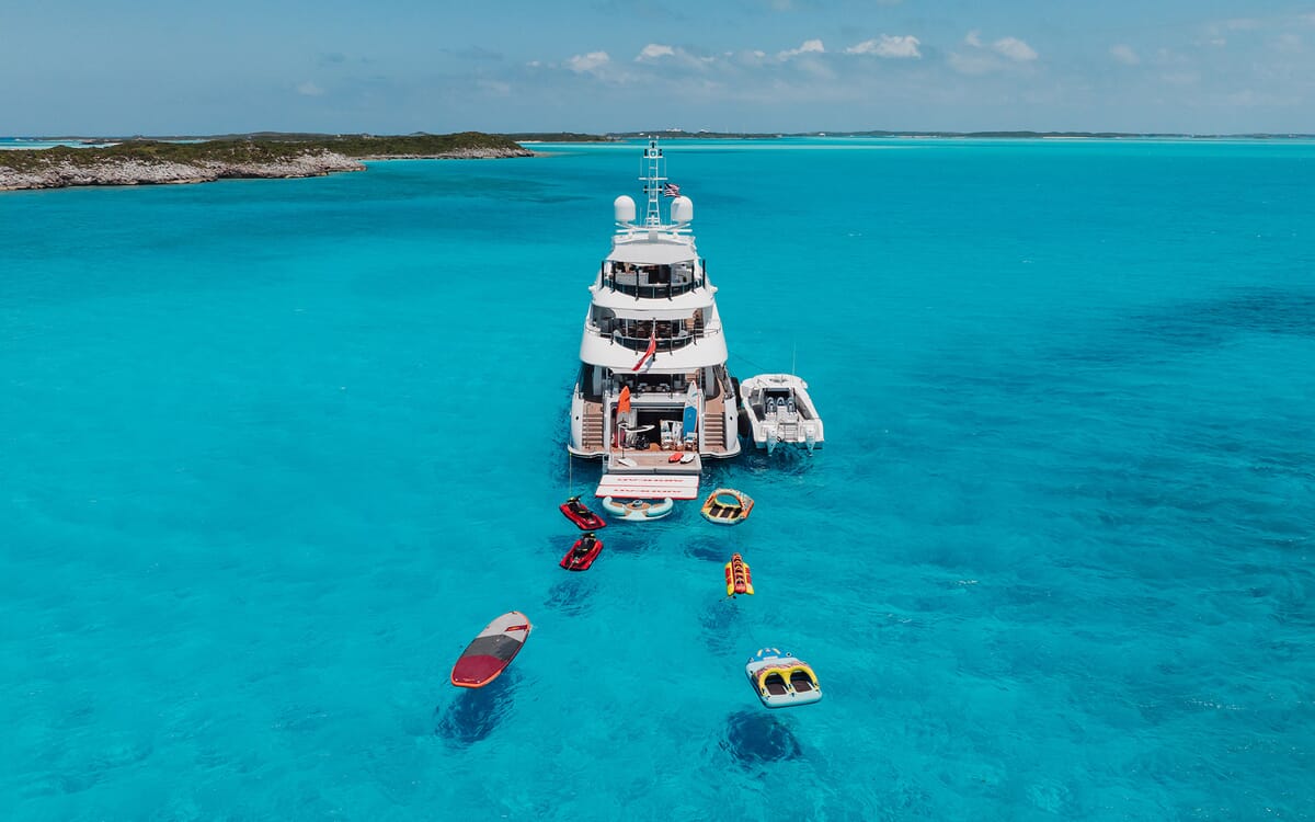 Luftaufnahme der 46,71 m langen Yacht ODYSSEA in türkisfarbenem Wasser, umgeben von Wasserspielzeug. Die Yacht ist angedockt und hat mehrere Decks.