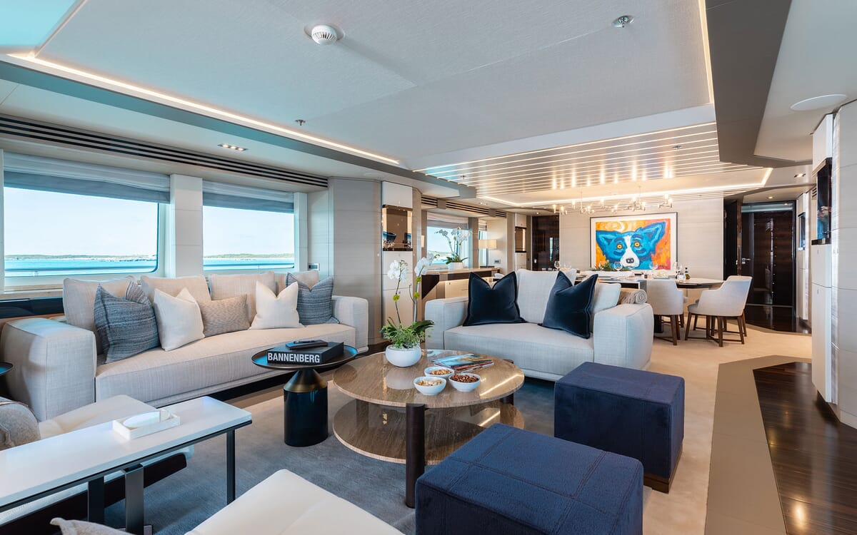 Innenansicht des Wohnbereichs der ODYSSEA Yacht mit bequemen Sitzgelegenheiten, einem Couchtisch und Kunstwerken, mit Blick auf das Meer durch die Fenster.