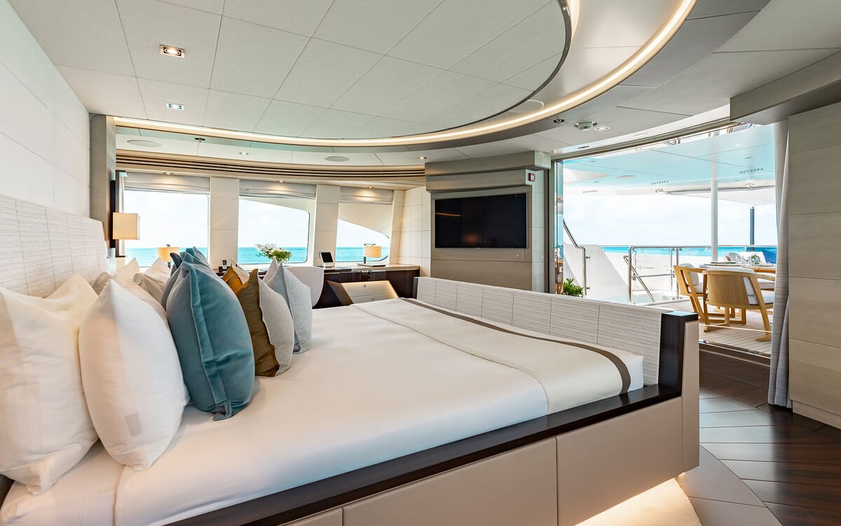 Innenansicht des Hauptschlafzimmers der ODYSSEA Yacht mit einem großen Bett und offenem Zugang zu einem Sitzbereich im Freien mit Blick auf das Meer.